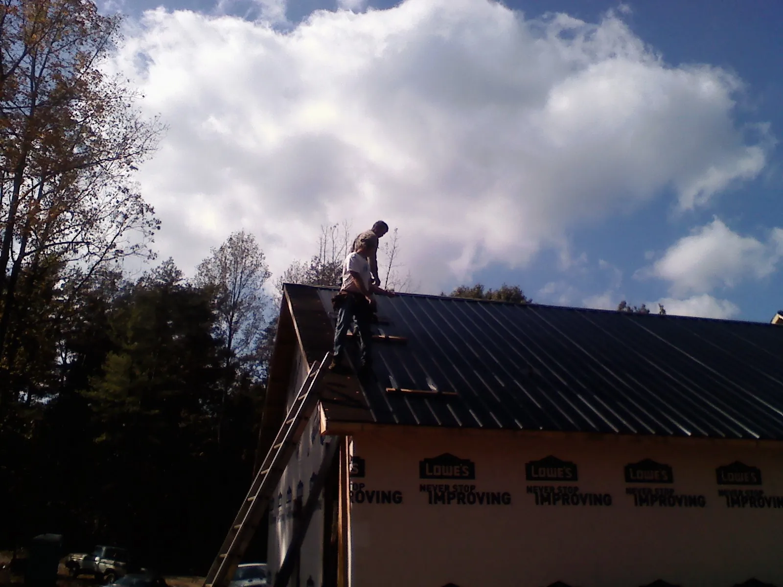Roofer fastening dark metal panels high against a cloudy sky, from a Roof Inspection job in Bremerton