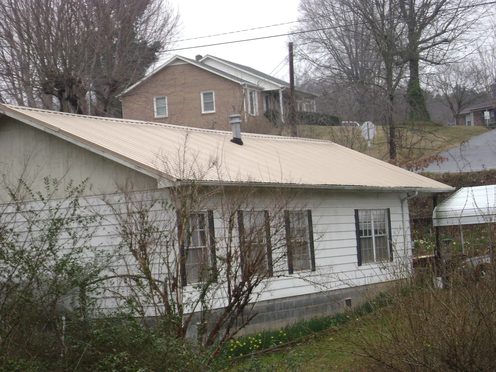 Tan metal roof on a white sided house set into a hillside — Commercial Roofing by Roofing Brothers in Bremerton